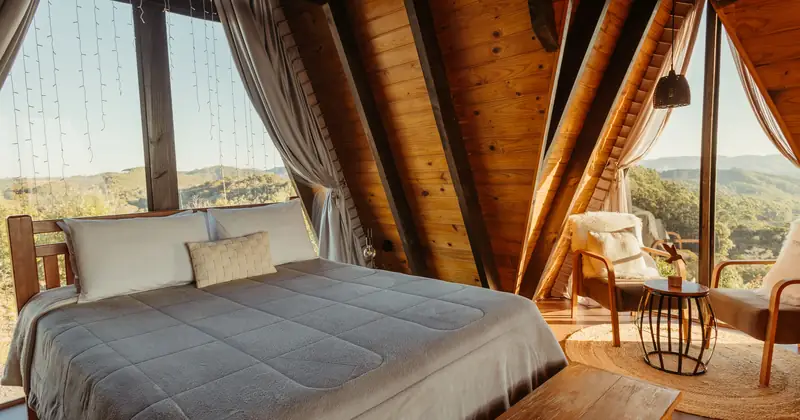 Spacious wooden A-frame bedroom featuring a large bed, cozy chairs, and a stunning mountain view.
