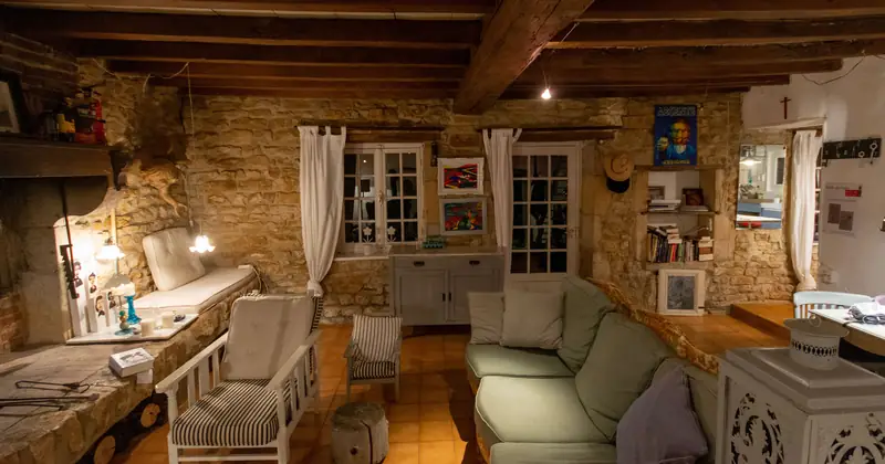 Warm rustic living room with stone walls, wooden beams, armchairs, and sofa creating a cozy ambiance.